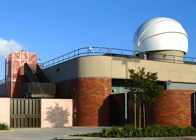 Modern observatory building with a large white dome under a clear blue sky.