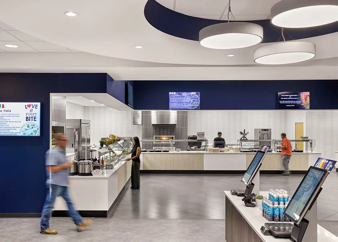 Modern cafeteria with people using self-service stations under stylish lighting.