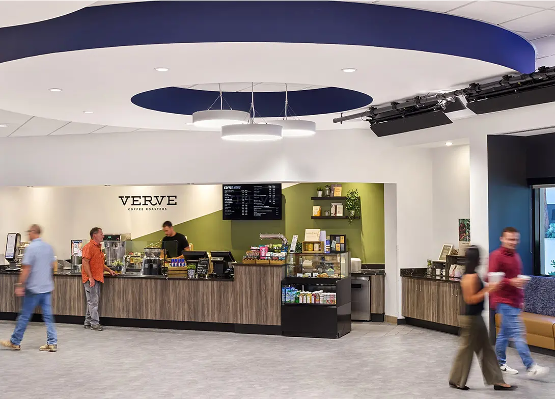 Modern coffee shop interior with green accents, menu board, and busy baristas serving customers.