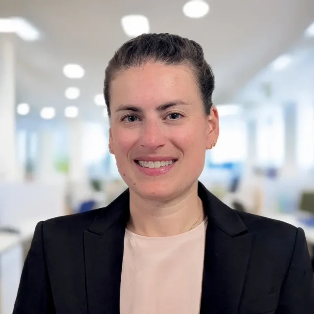 Business professional smiling in an office setting with blurred background.