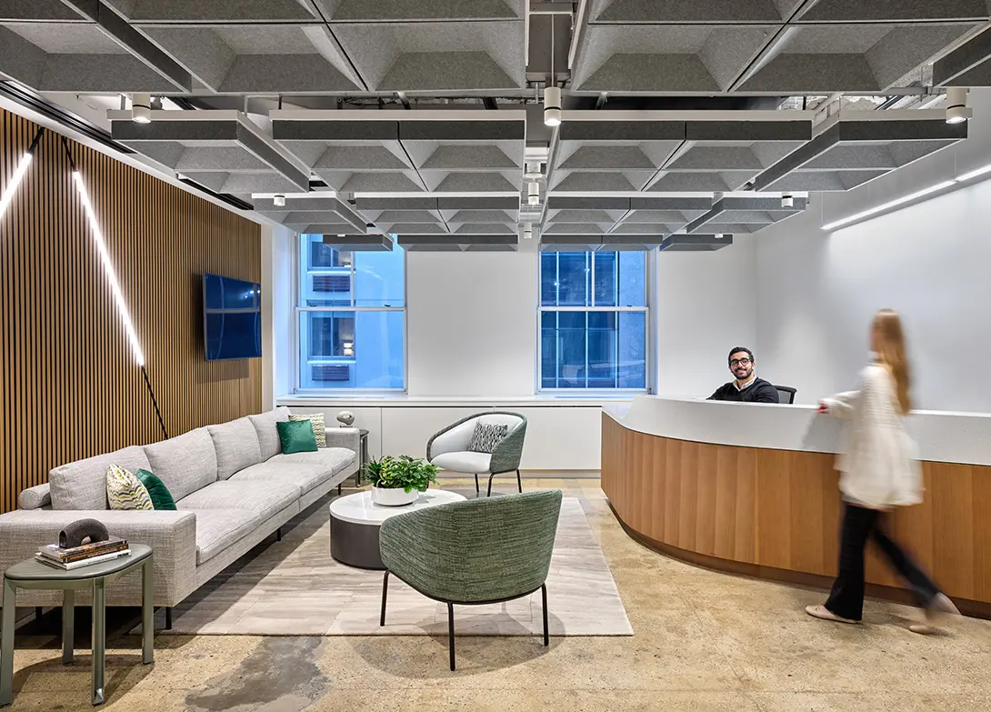 Modern office reception with stylish seating, wood accents, and acoustic ceiling panels for a welcoming environment.