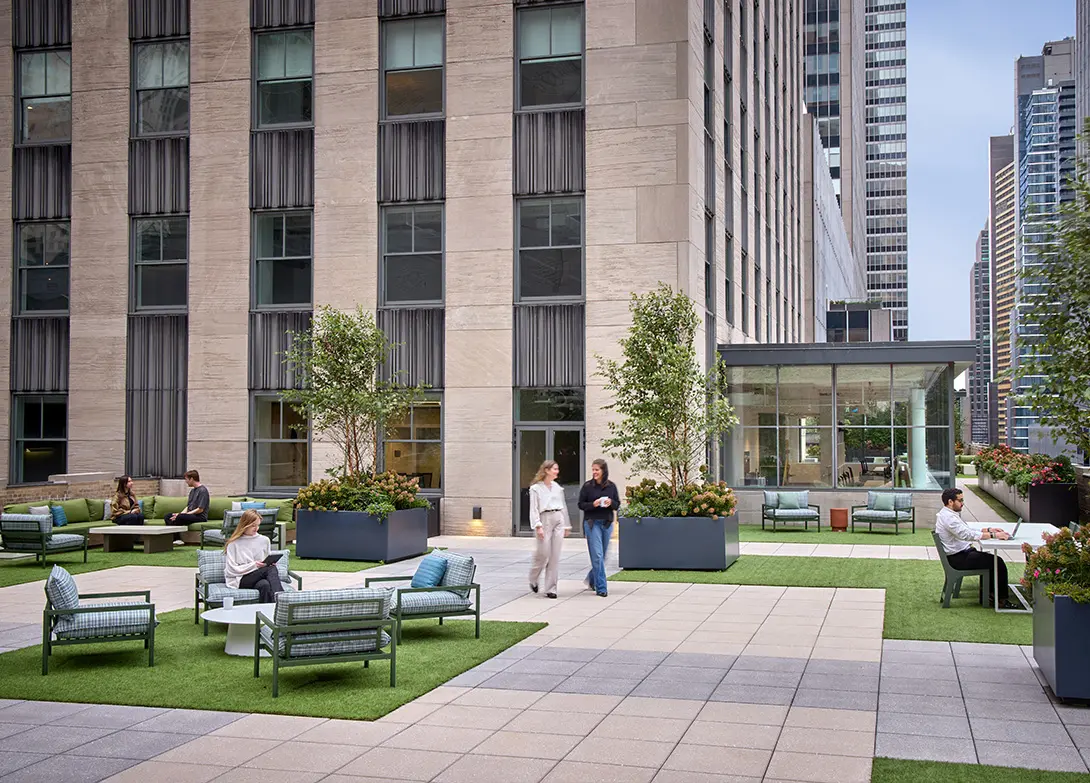 Modern office terrace with people relaxing and working, featuring greenery and outdoor seating in an urban setting.