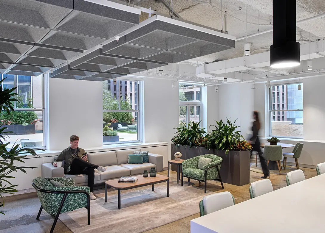 Modern office lounge with plants, sofas, and large windows creating a welcoming work environment.