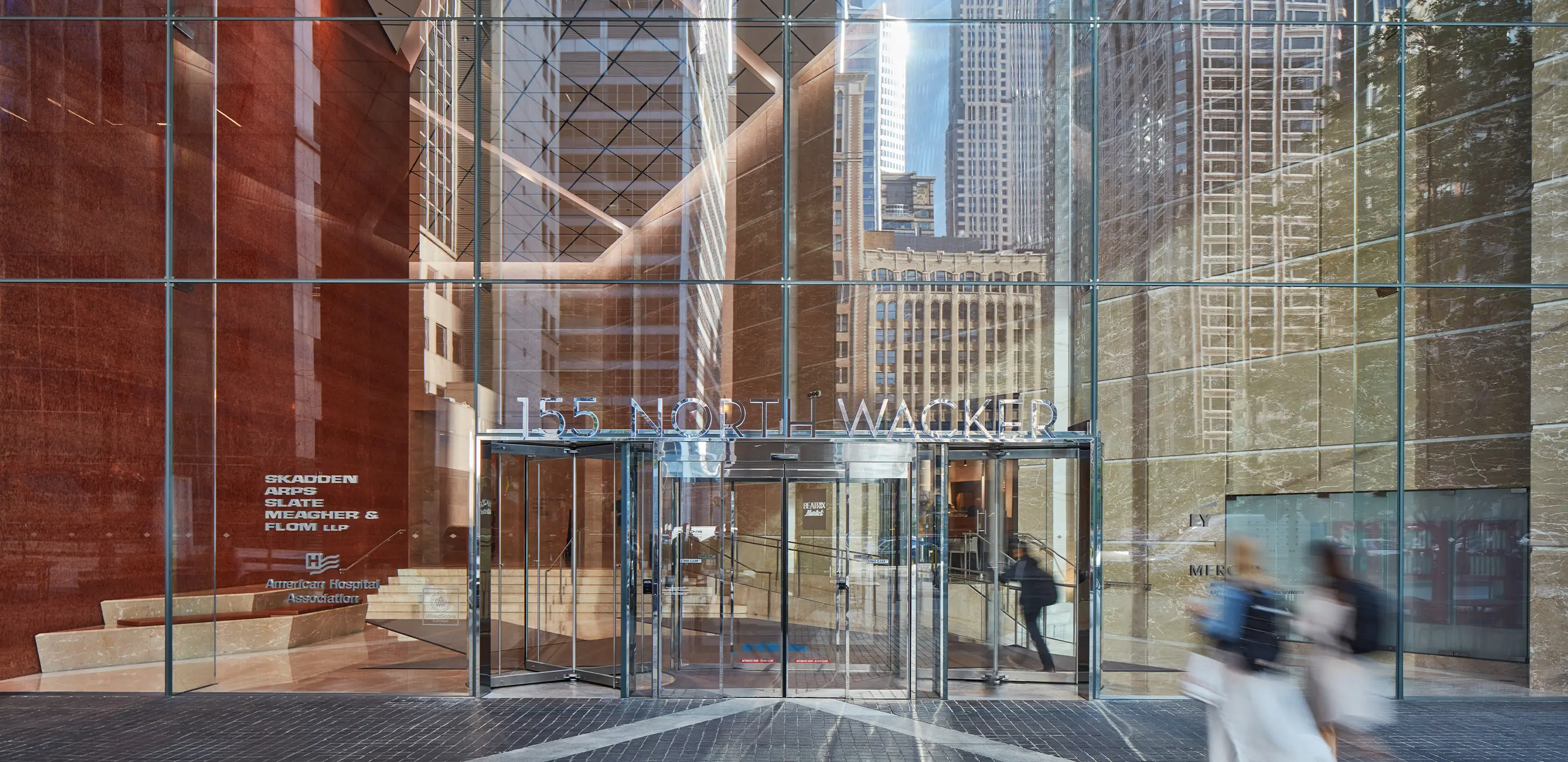 Exterior view of 155 North Wacker entrance, featuring reflections of surrounding skyscrapers and busy foot traffic.