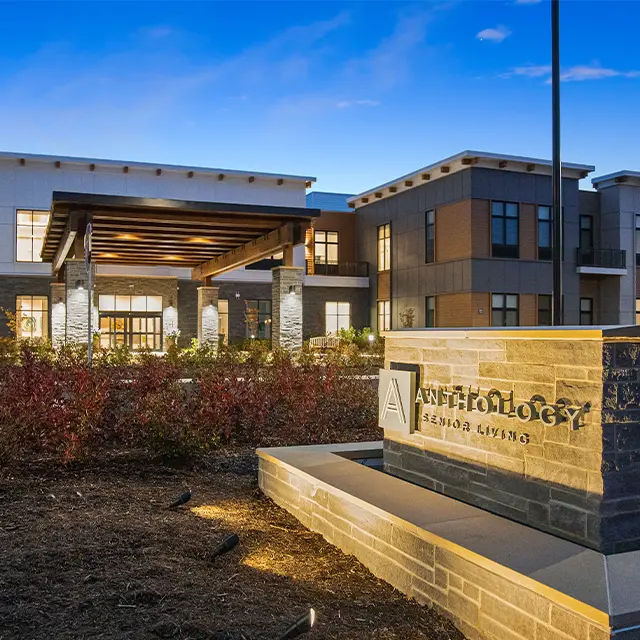 Elegant senior living facility exterior at dusk with stone signage and well-lit entrance.
