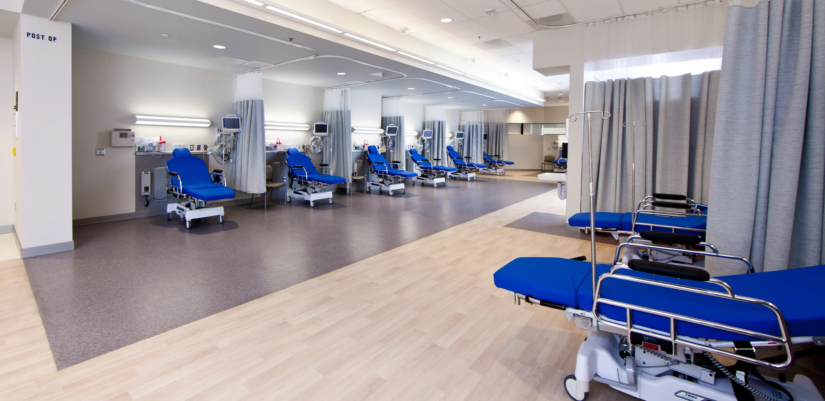 Modern hospital recovery room with multiple blue patient beds and medical equipment.