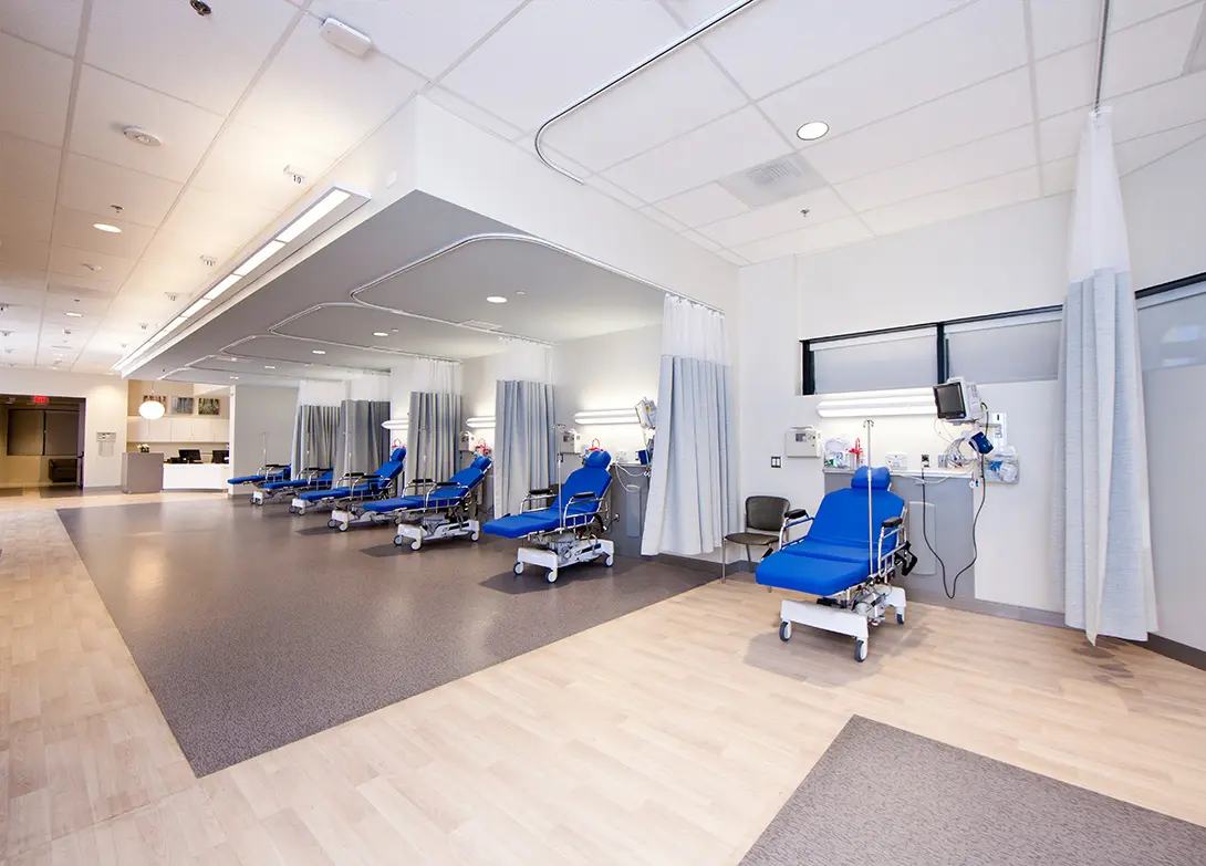Modern hospital infusion room with blue recliners and medical equipment.