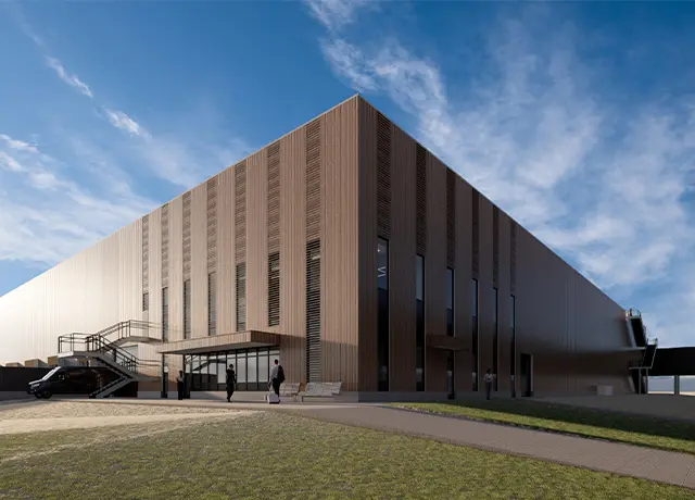 Modern industrial building with wood panel facade, featuring people and cars outside, under a clear blue sky.