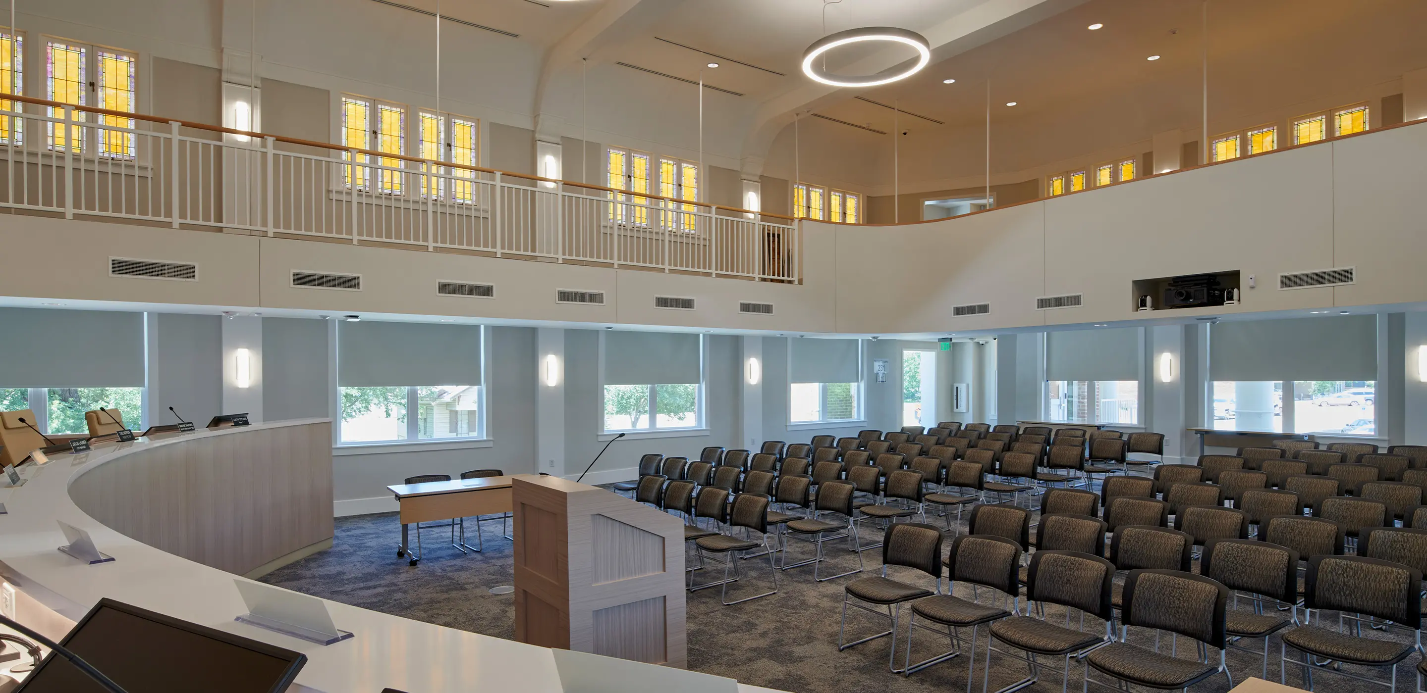 Modern conference room with curved podium, rows of chairs, and natural lighting from large windows.