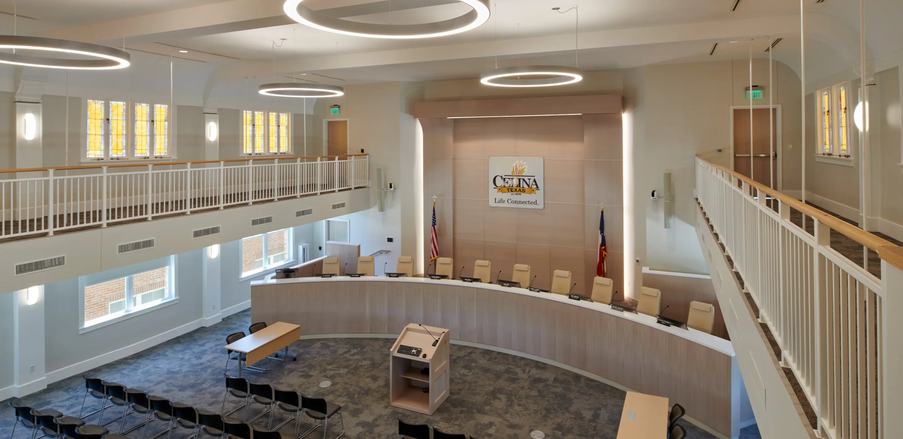 Modern council chamber with a curved table, podium, and a sign, illuminated by circular lights.