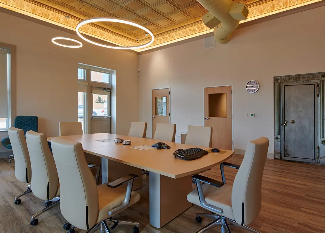 Modern conference room with beige chairs, circular ceiling lights, and a large wooden table in an office setting.