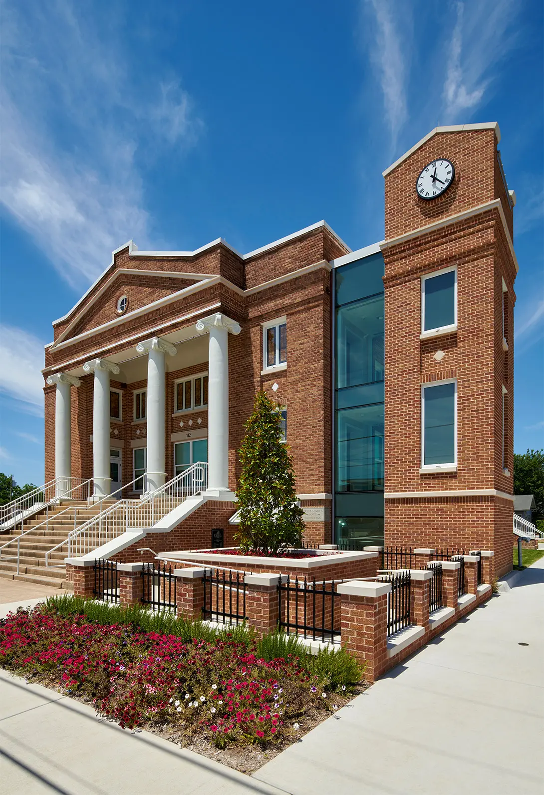 Historic brick courthouse with clock tower, framed by blue sky and flowerbed, showcasing classic architecture.