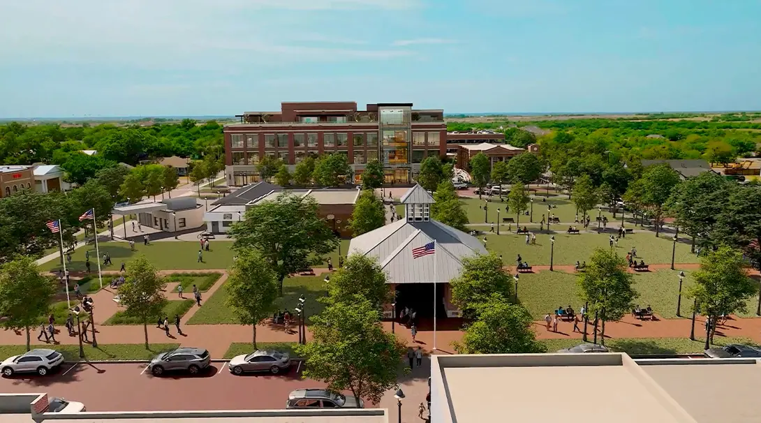 Aerial view of a park with pavilion, modern building, and green trees under a clear blue sky.