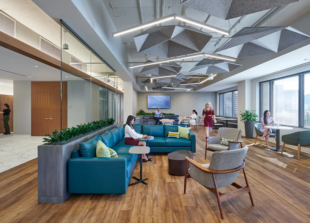 Modern office lounge with comfortable seating, geometric ceiling design, and people working on laptops.
