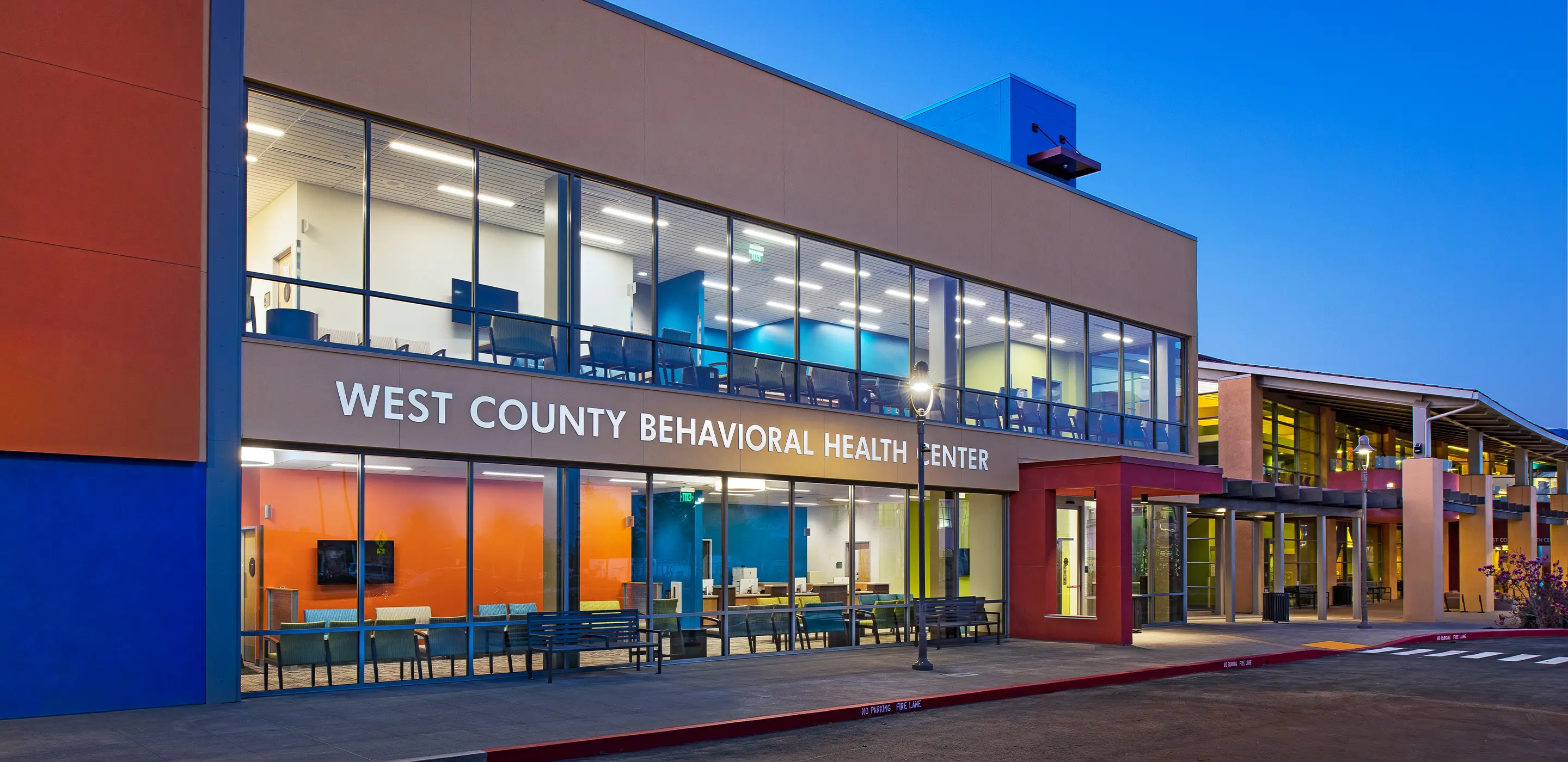Modern exterior of West County Behavioral Health Center illuminated at dusk.