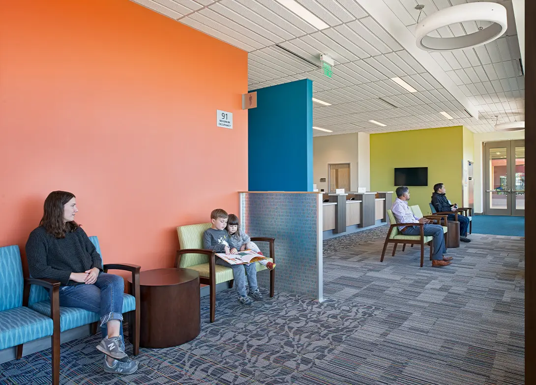 Modern waiting room with colorful walls, seating area, and people sitting and reading.