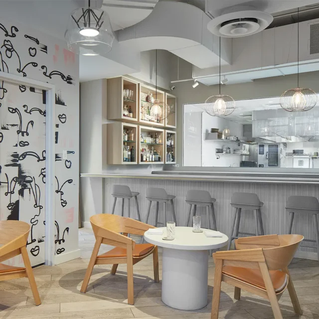 Modern restaurant interior with bar stools, artistic wall design, and wooden chairs around a small table.