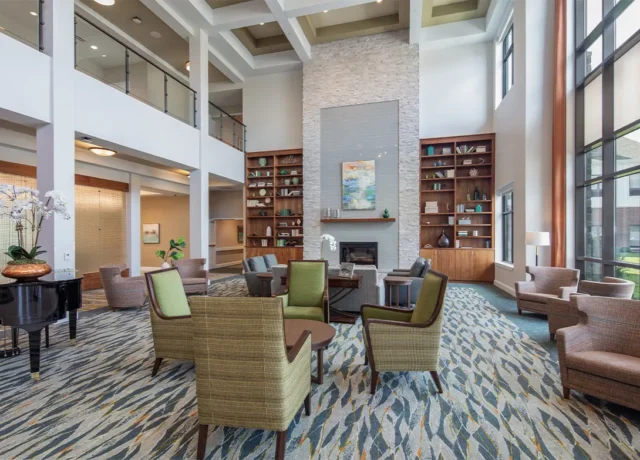 Modern hotel lobby with tall ceilings, stylish seating, large shelves, and a cozy fireplace.