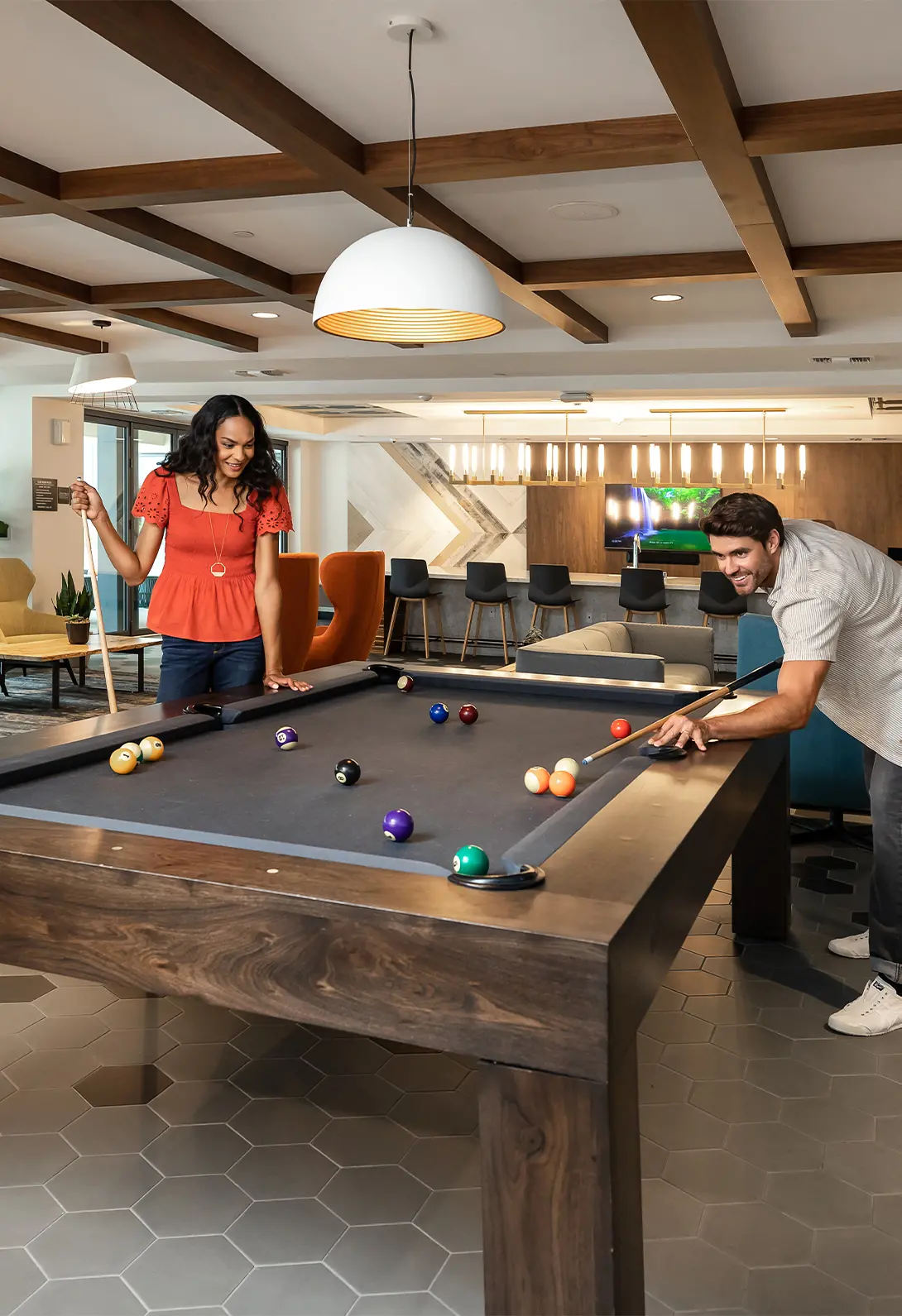 Two people playing pool in a modern recreational room with stylish decor and ceiling lights.