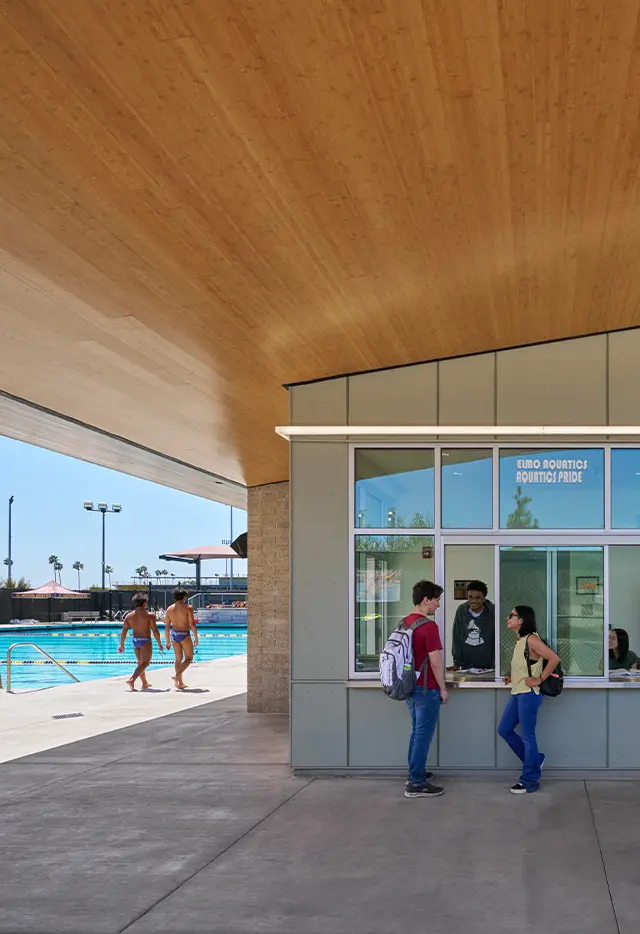 Modern aquatics center with students talking at a service window, swimmers by the pool.