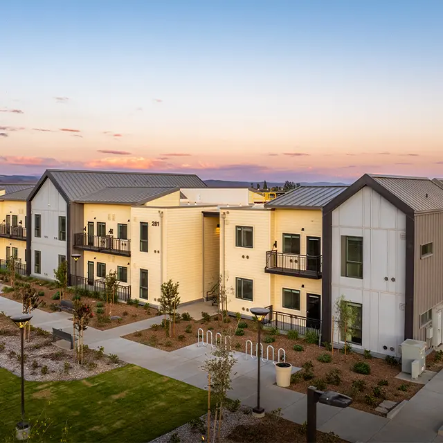 Modern apartment complex at sunset with landscaped grounds and pathways.