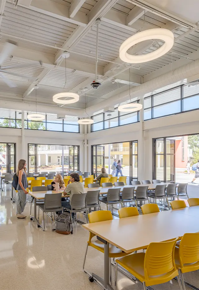 Modern cafeteria with yellow chairs, large windows, and circular ceiling lights, fostering a bright and open atmosphere.