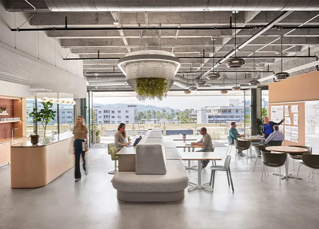 Modern open office space with collaborative seating, people working, large windows, and green ceiling decor.
