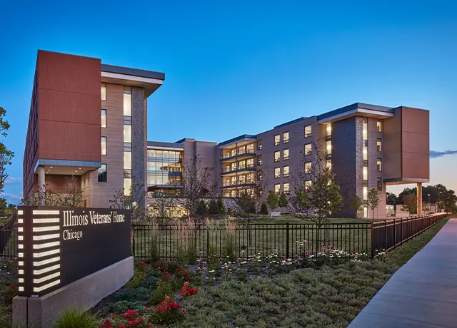 Modern exterior of Illinois Veterans' Home in Chicago at dusk, featuring landscaped gardens and illuminated windows.