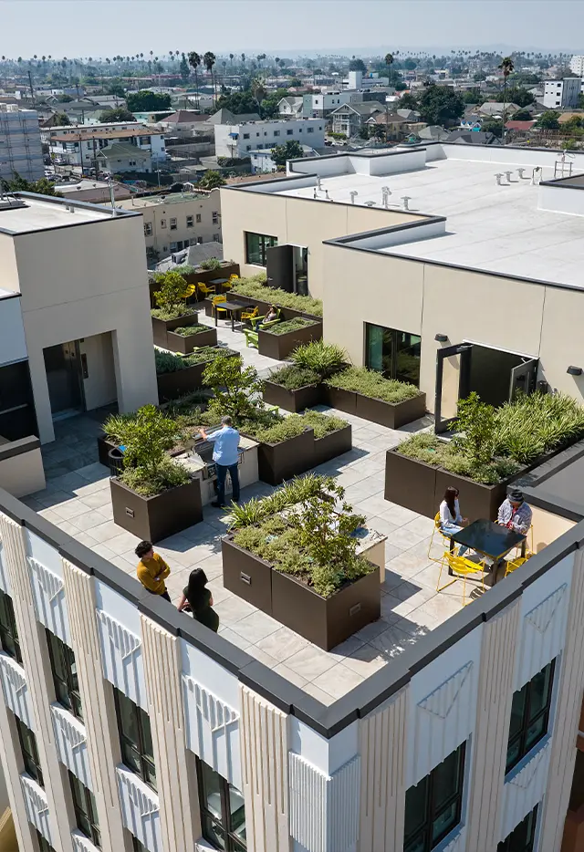 Rooftop garden with people relaxing and dining, overlooking a cityscape on a sunny day. Urban outdoor space.