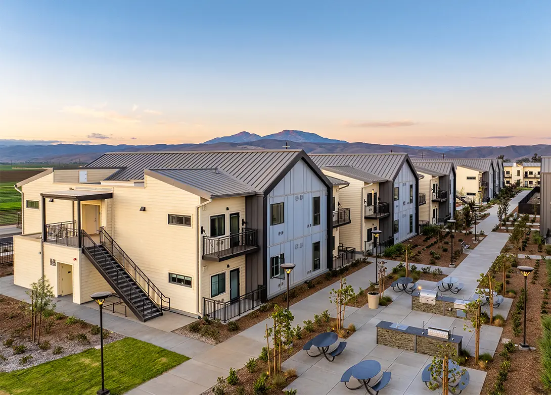 Modern apartment complex with mountain views, outdoor seating, and landscaped gardens at sunset.