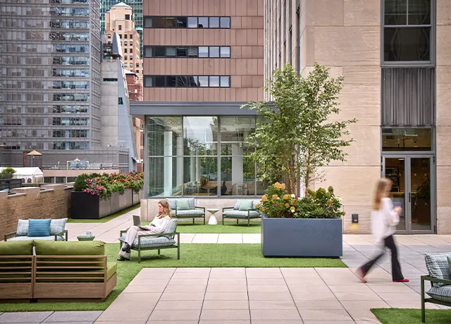 Rooftop garden with modern seating and plants, surrounded by city buildings, featuring a relaxing outdoor setting.