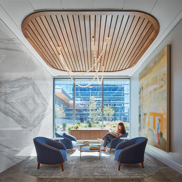 Modern lounge area with blue chairs, wooden ceiling, and artwork near large window with city view.