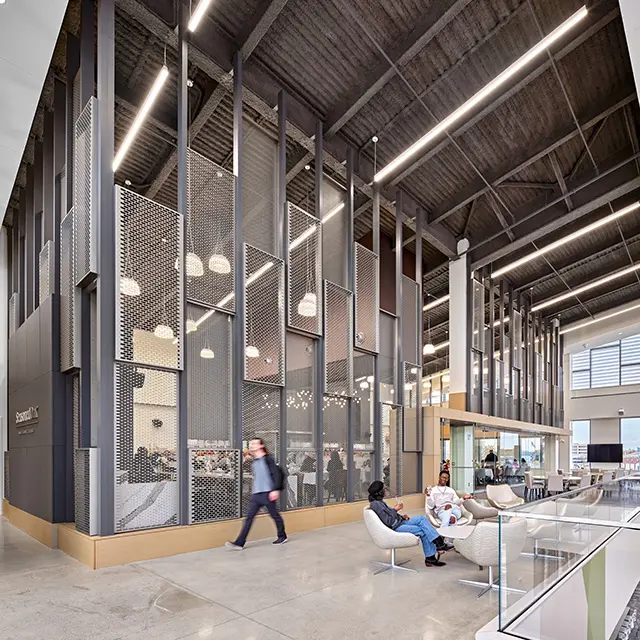 Modern office lobby with people seated and industrial design elements, including high ceilings and mesh panels.