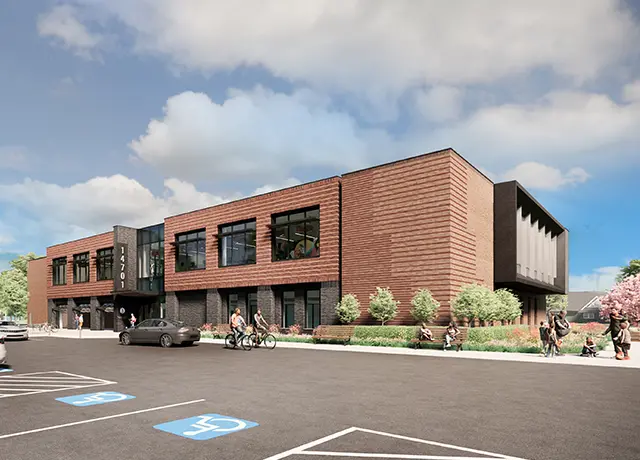 Modern brick building with large windows, people outside, greenery, and accessible parking spaces in the foreground.