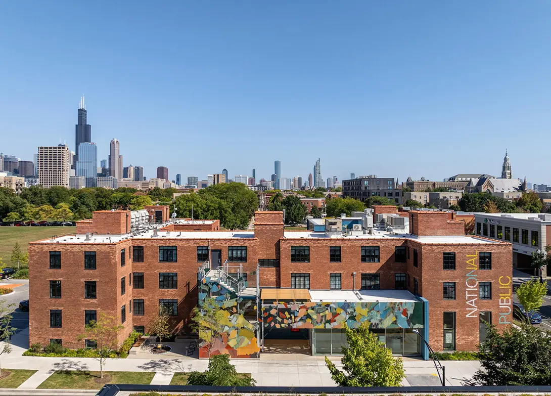Red brick building in urban landscape with city skyline in the background, under clear blue sky.
