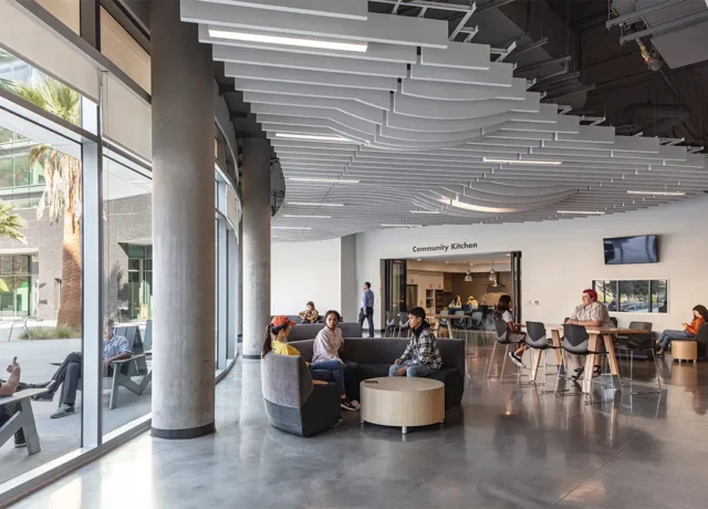 Modern community kitchen interior with people seated, featuring stylish ceiling design and large windows.