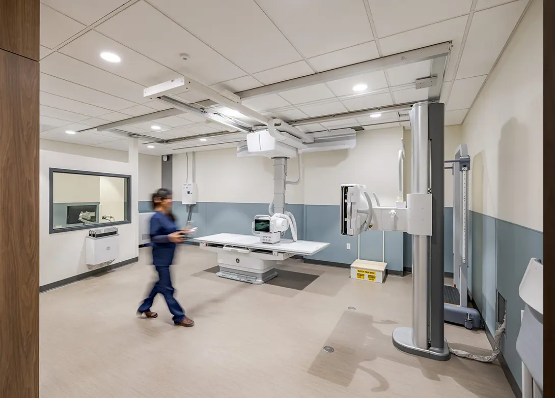 Modern radiology room with medical equipment and healthcare professional in motion.
