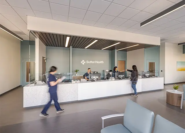 Modern reception area of a healthcare facility with staff and visitors at the front desk.