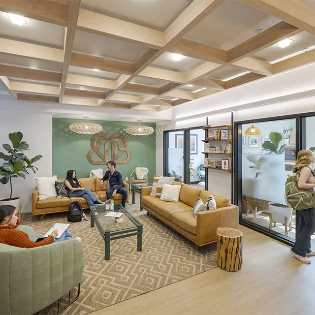 Modern coworking space with people relaxing on couches, wood decor, and plants, fostering collaboration and comfort.