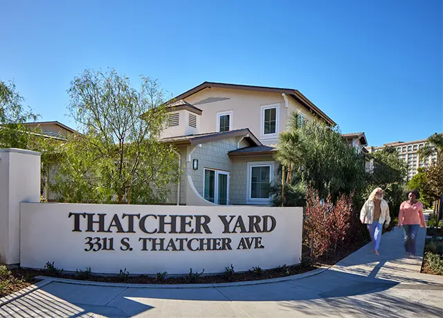 Thatcher Yard entrance with address, two people walking, modern residential building, and clear blue sky.