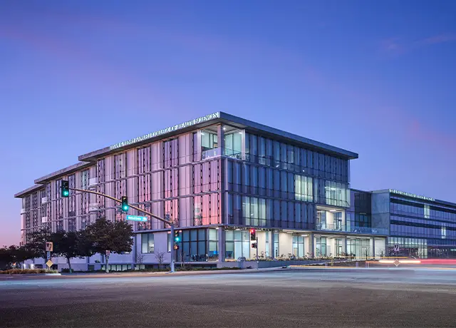 Modern glass office building at twilight with glowing windows and streetlights, capturing urban architecture.