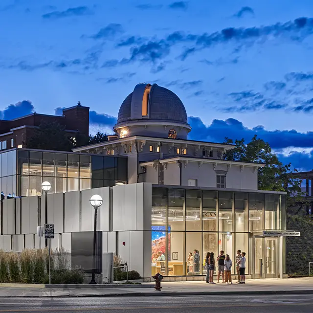 Modern observatory building at dusk with lit interior and blue sky background.