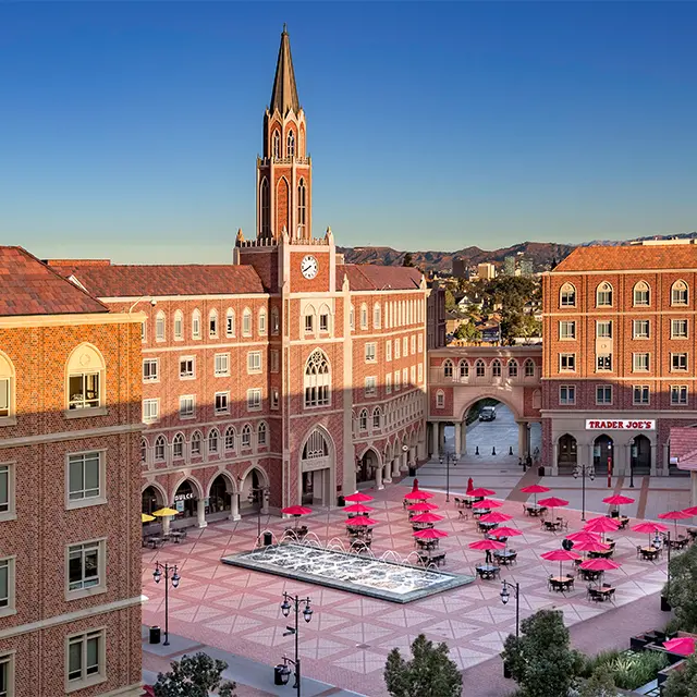 Scenic view of a university courtyard with fountain, red umbrellas, and historic buildings under a clear blue sky.