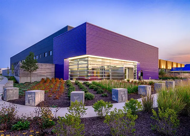 Modern purple building with large windows surrounded by landscaped gardens at sunset.