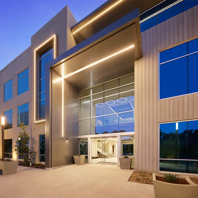 Modern office building facade with illuminated entryway and large glass windows at dusk.