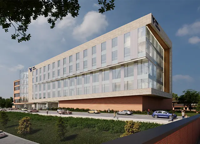 Modern six-story building with glass facade, cars parked outside, and people walking on a sunny day.