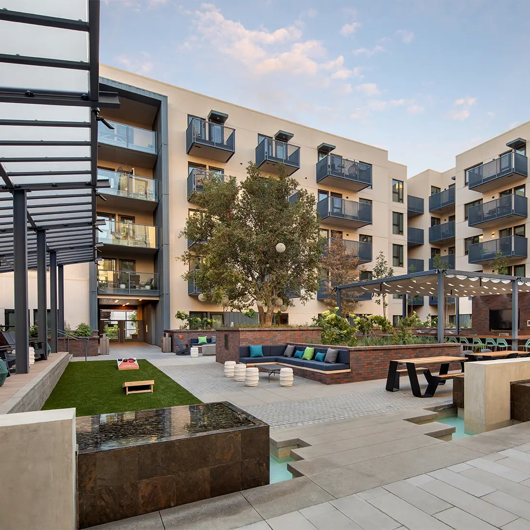Modern apartment courtyard with seating, green lawn, and balconies, under a blue sky. Ideal for relaxation and gatherings.
