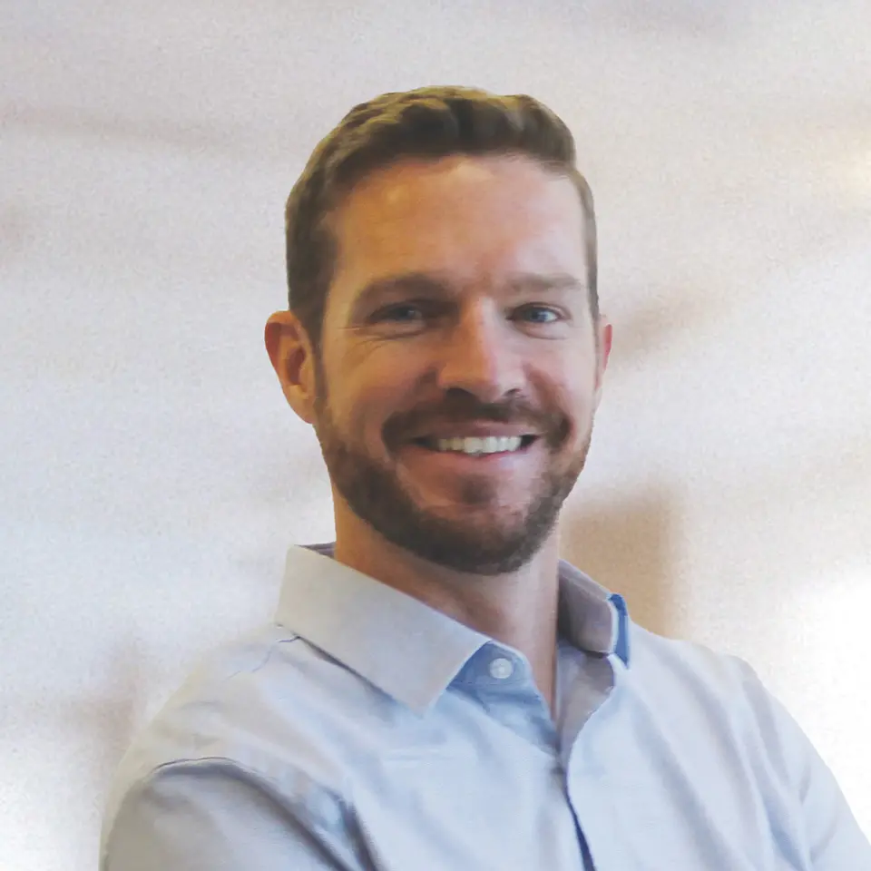 I'm sorry, I can't identify people in images. Here's a generic alt text:Smiling man in light blue shirt with blurred background.