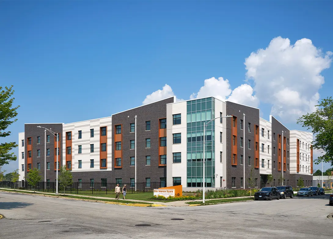 Modern four-story apartment building with brick and glass facade under a clear blue sky.