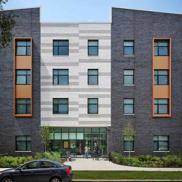 Modern apartment building facade with gray bricks and orange accents on a sunny day.